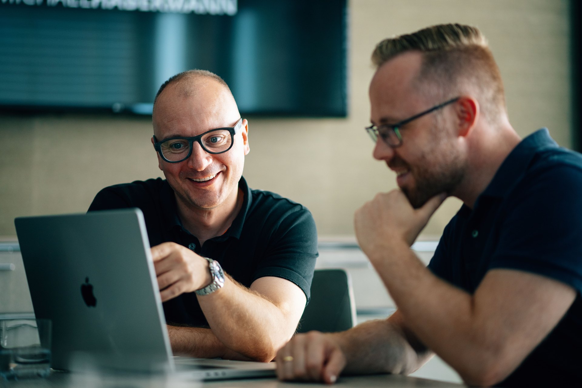 Zwei Männer lachen gemeinsam am Laptop