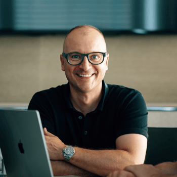 Lächelnder Mann mit Brille und schwarzem Poloshirt am Laptop