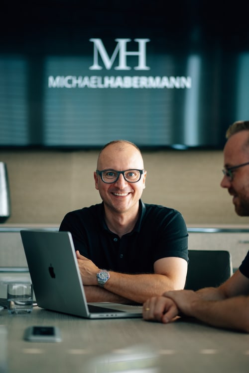 Zwei Männer am Laptop in einem Büro, im Hintergrund das Logo Michael Habermann