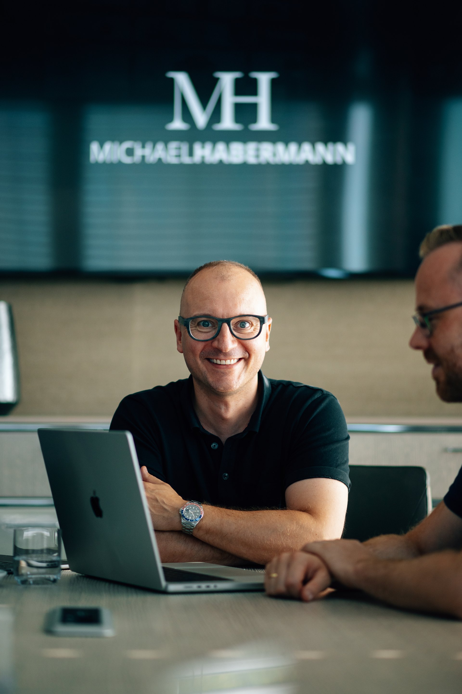 Zwei Männer am Laptop in einem Büro, im Hintergrund das Logo Michael Habermann