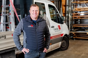 Mann in Steppjacke vor einem Transporter der T. Knöbl Dachdeckerei